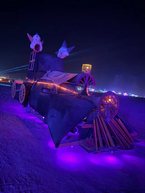 Front of the art car with its cowcatcher, wagon wheels and clown heads glowing purple